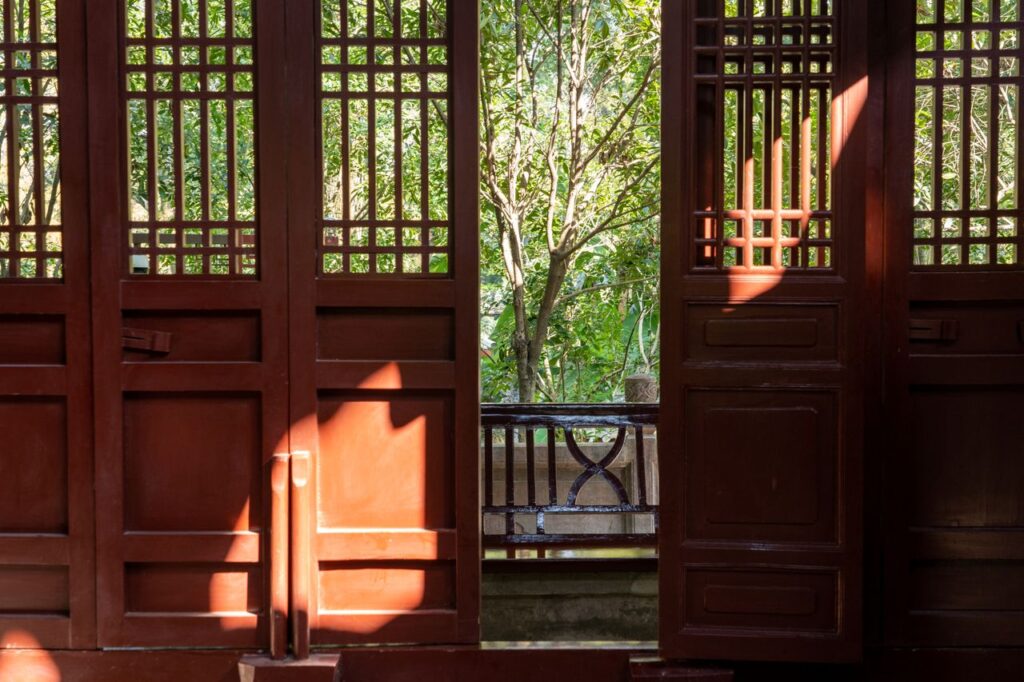 Sunlight streaming through a traditional wooden doorway, revealing lush green trees outside.